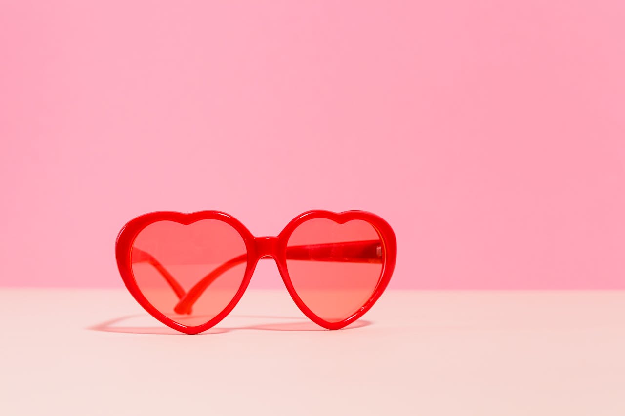 gallery-img-03 Red heart-shaped sunglasses on a pastel pink backdrop, perfect for Valentine's Day themes.