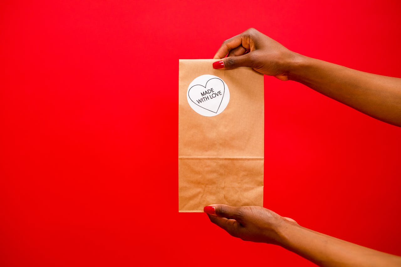 gallery-img-02 Brown paper bag with 'Made With Love' label held by hands over a red background.